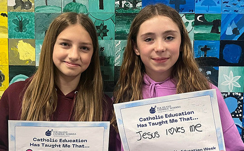 Two students holding signs that share what Catholic Education has taught them.